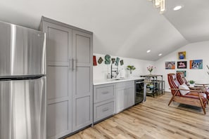 A modern kitchen with grey cabinets, a stainless steel refrigerator, and a dining area with a wooden floor and a brown leather chair.