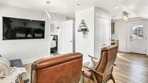 Una sala de estar moderna con un televisor de pantalla plana, sillas de cuero, una zona de comedor y una cocina al fondo.