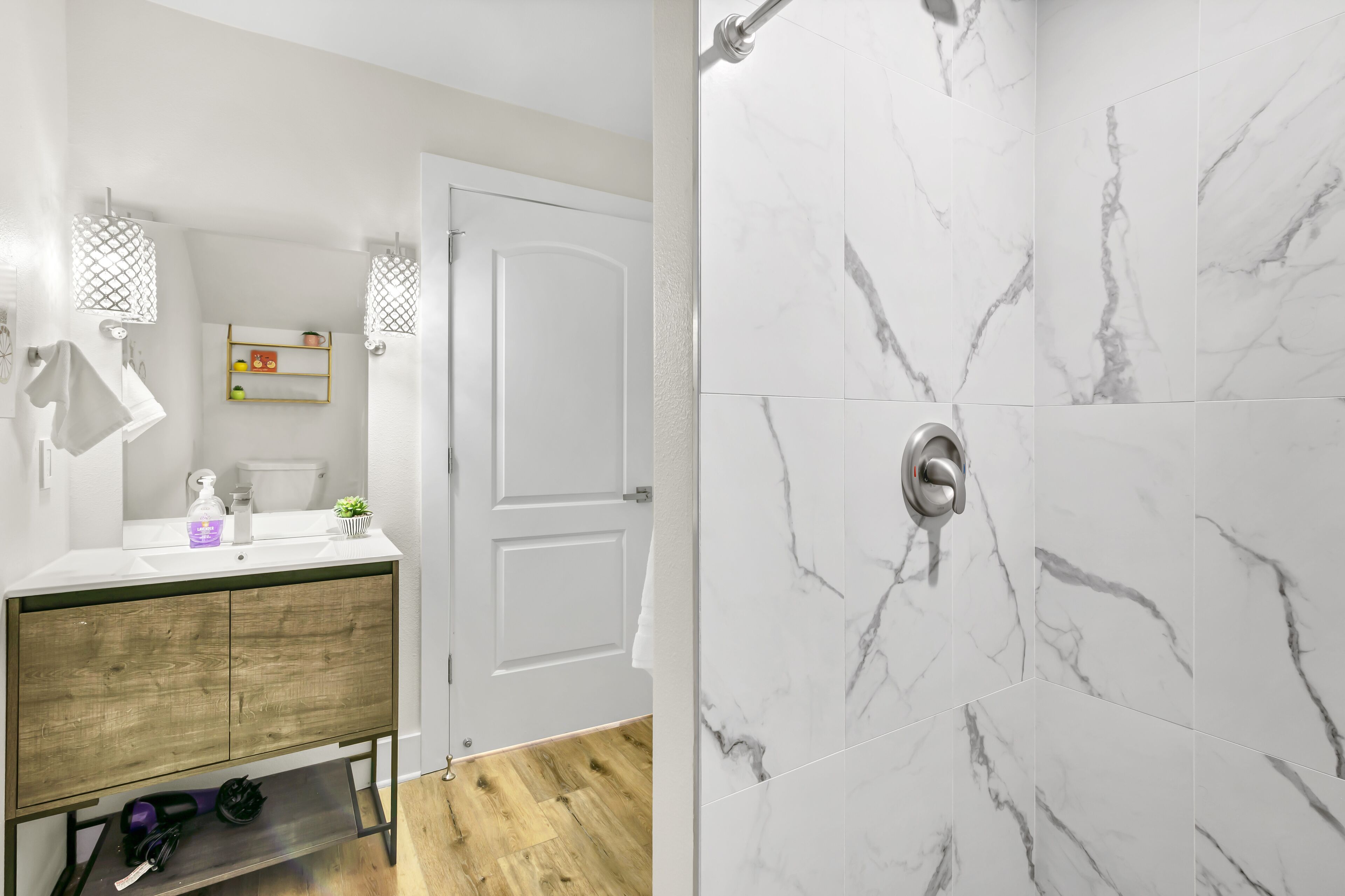 A bathroom with a wooden vanity, white sink, and marble shower walls.