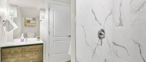 A bathroom with a wooden vanity, white sink, and marble shower walls.