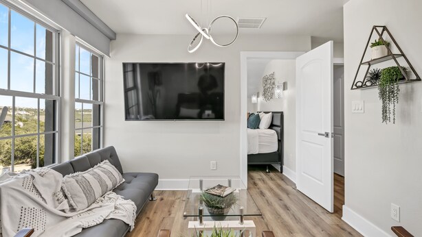 Una sala moderna con un sofá gris, una mesa de centro de vidrio y un televisor grande en la pared.