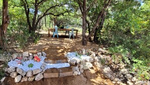 Un espacio de estar al aire libre rústico con una mesa y sillas de madera, rodeado de piedra natural y follaje.