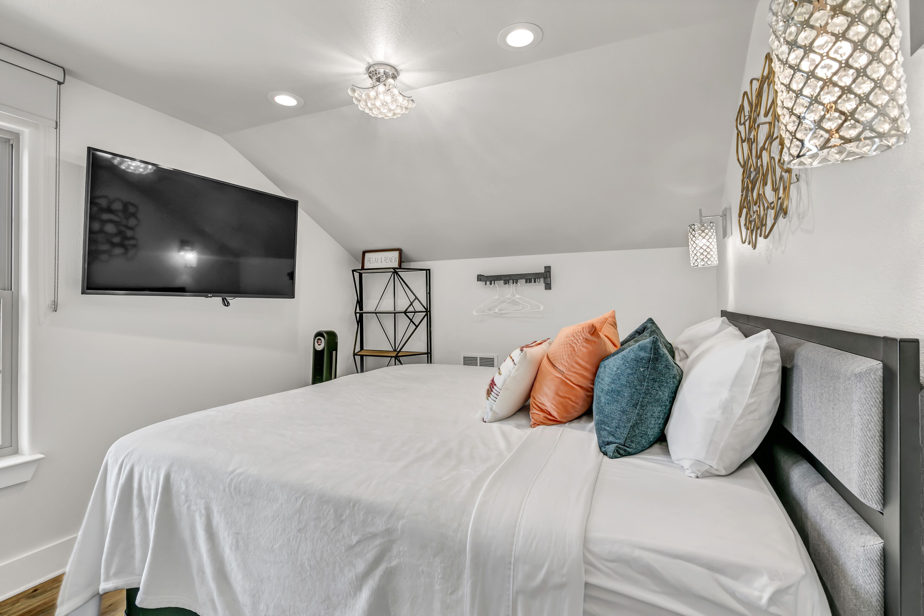 A modern bedroom with a large bed, a flat-screen TV mounted on the wall, and a unique geometric light fixture.