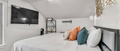 A modern bedroom with a large bed, a flat-screen TV mounted on the wall, and a unique geometric light fixture.