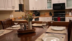 A dining area with a wooden table set for four, white cabinets, a black microwave, and a chandelier. - Woodsy Escape Located south of Kalispell Montana (Kalispell)