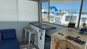 A compact living space with a kitchenette, a blue sofa, and a view of boats through large windows.