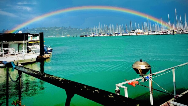 A marina with boats docked, a rainbow in the sky, and a clear view of the water.