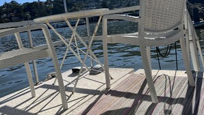 A boat deck with a white metal railing, a white plastic chair, and a patterned mat.