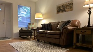 Een woonkamer met een bruine leren bank, een getextureerd vloerkleed en een lamp.
