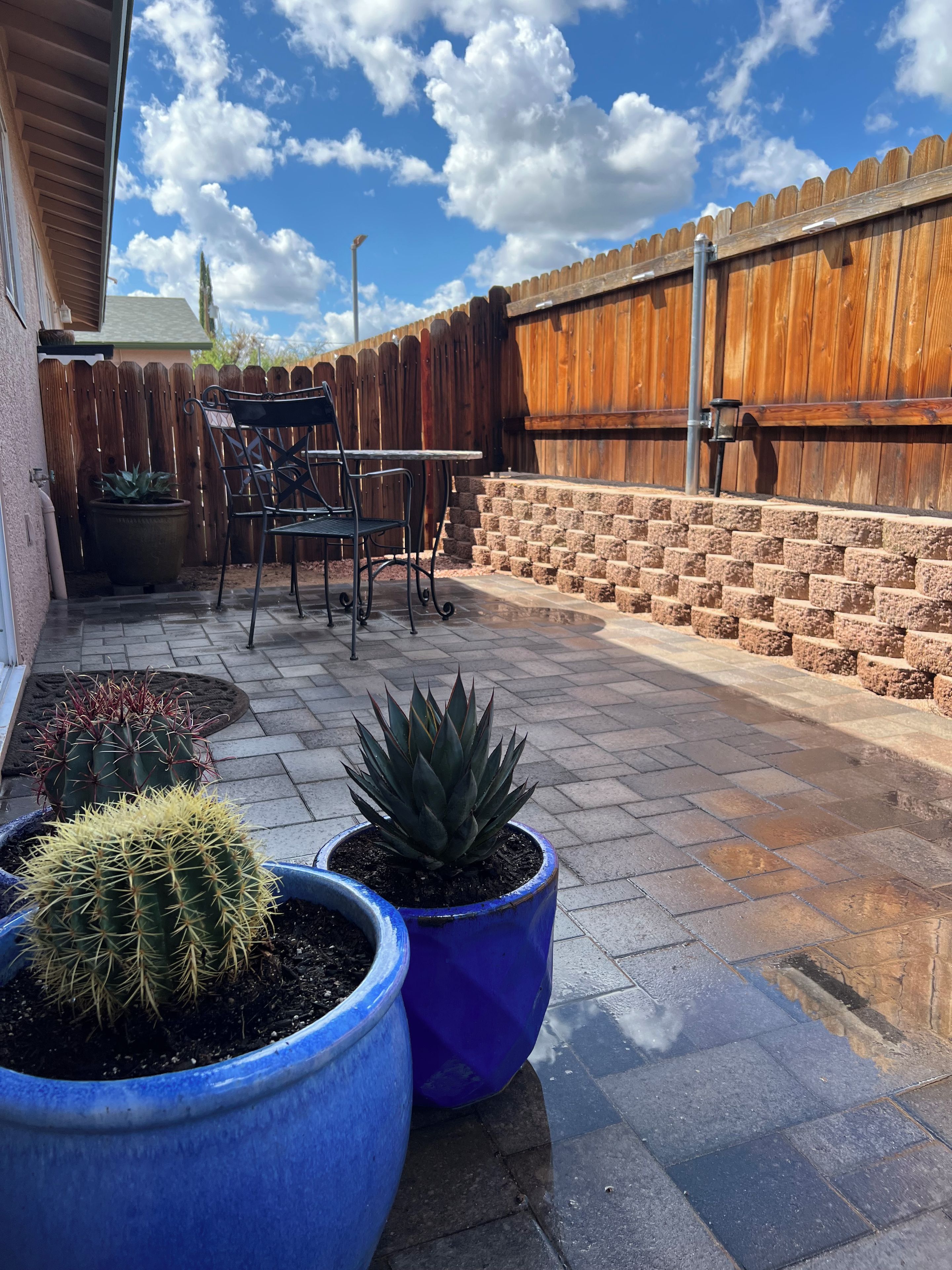 A patio area with a wooden fence, a table with chairs, and potted plants.