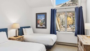 A hotel room with two beds, a window with curtains, a framed picture on the wall, and a wooden nightstand with a lamp. - Serenity at Cimarron Lodge! Hot Tub, Parking (Telluride)