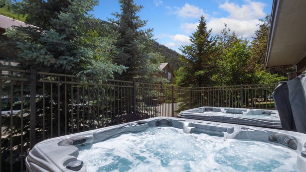 A hot tub area with a wooden fence, surrounded by trees and a mountain in the background. - Serenity at Cimarron Lodge! Hot Tub, Parking (Telluride)
