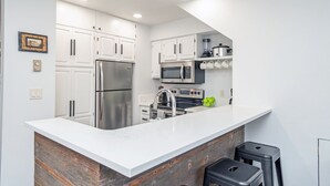 A modern kitchen with white cabinets, stainless steel appliances, a large island, and a wooden accent wall. - Serenity at Cimarron Lodge! Hot Tub, Parking (Telluride)