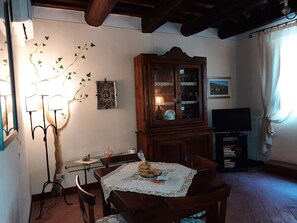 A dining area with a wooden table set for two, a cabinet with glass doors, a television, and a radiator.