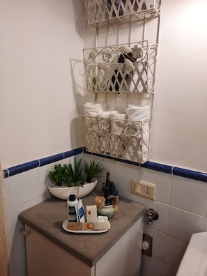 A bathroom with a white sink, a towel rack with multiple towels, a potted plant, and toiletries on the counter.