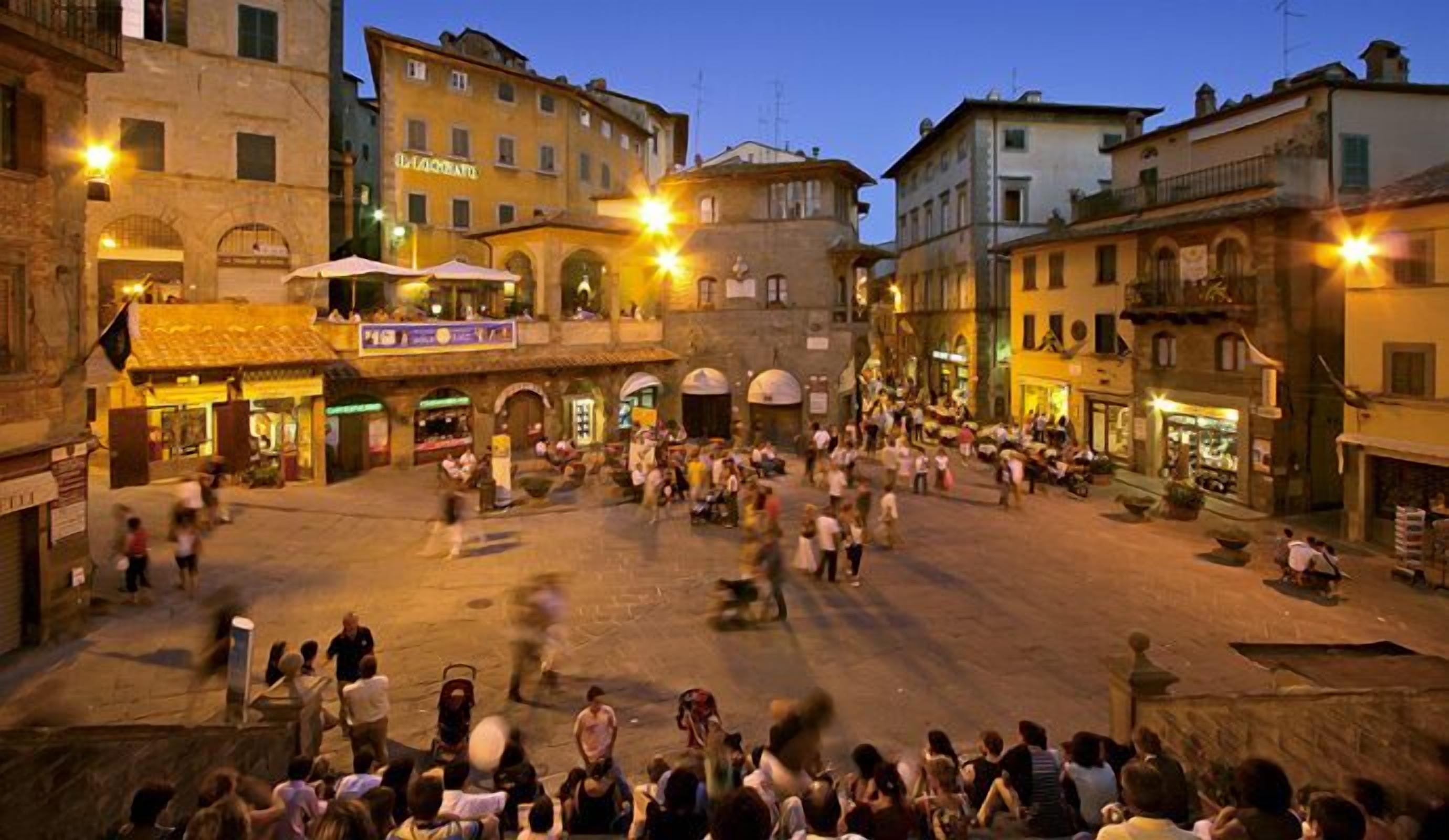 A bustling square with historic buildings, outdoor seating, and a crowd of people.