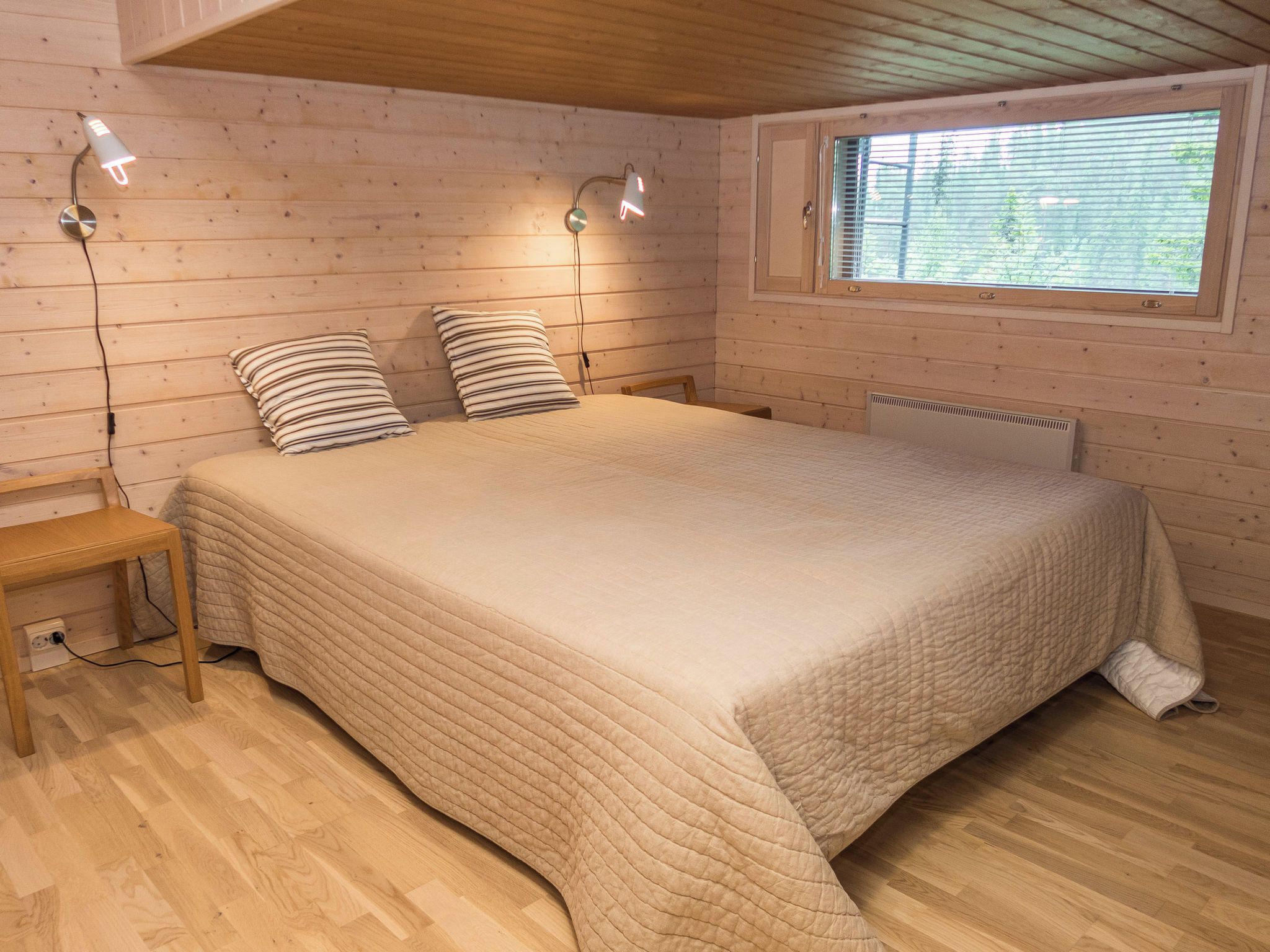 Une chambre avec un grand lit, deux lampes de chevet, une fenêtre et un banc en bois.