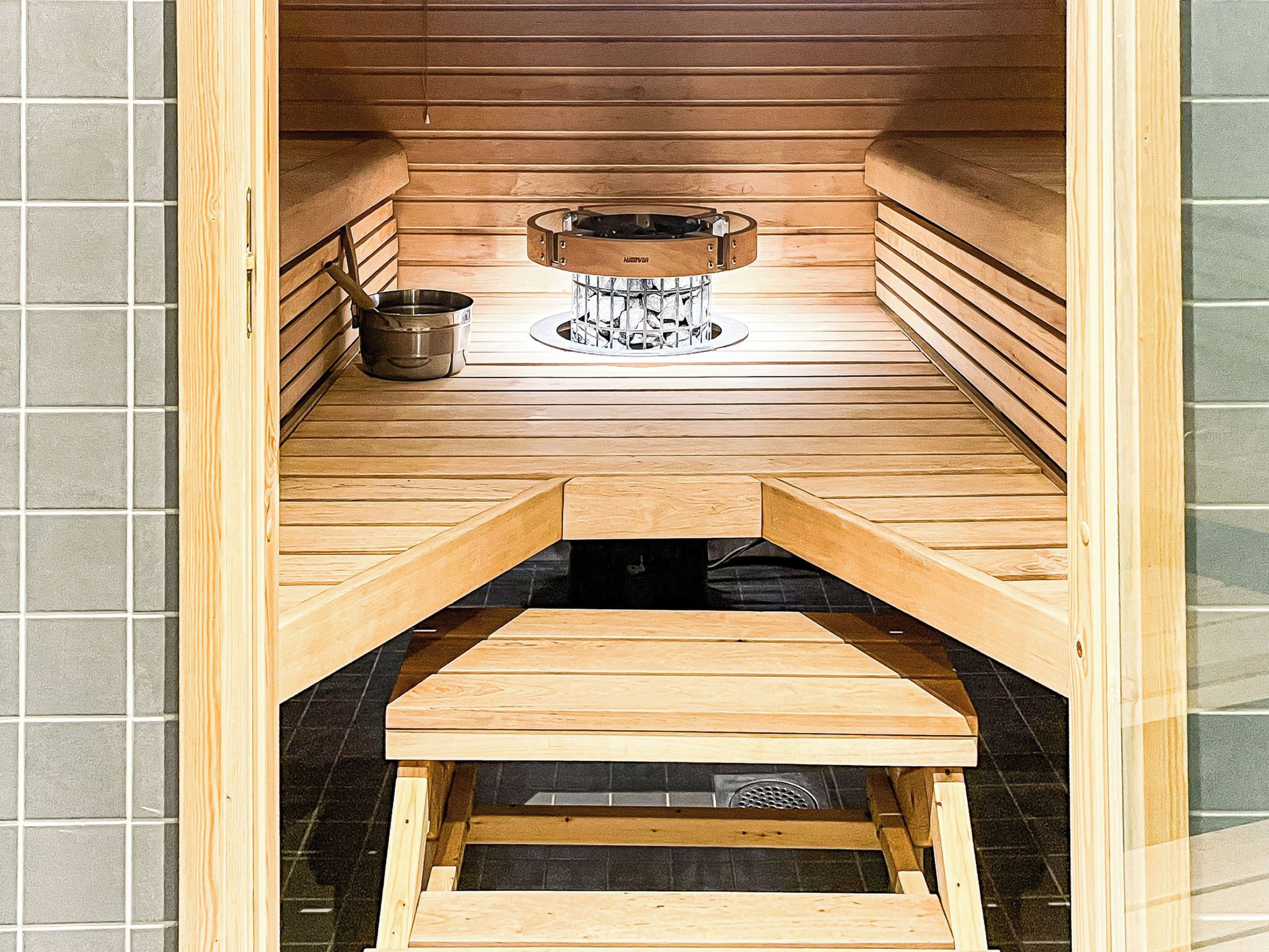 A sauna with a wooden bench, a metal container, and a heat source in the center.