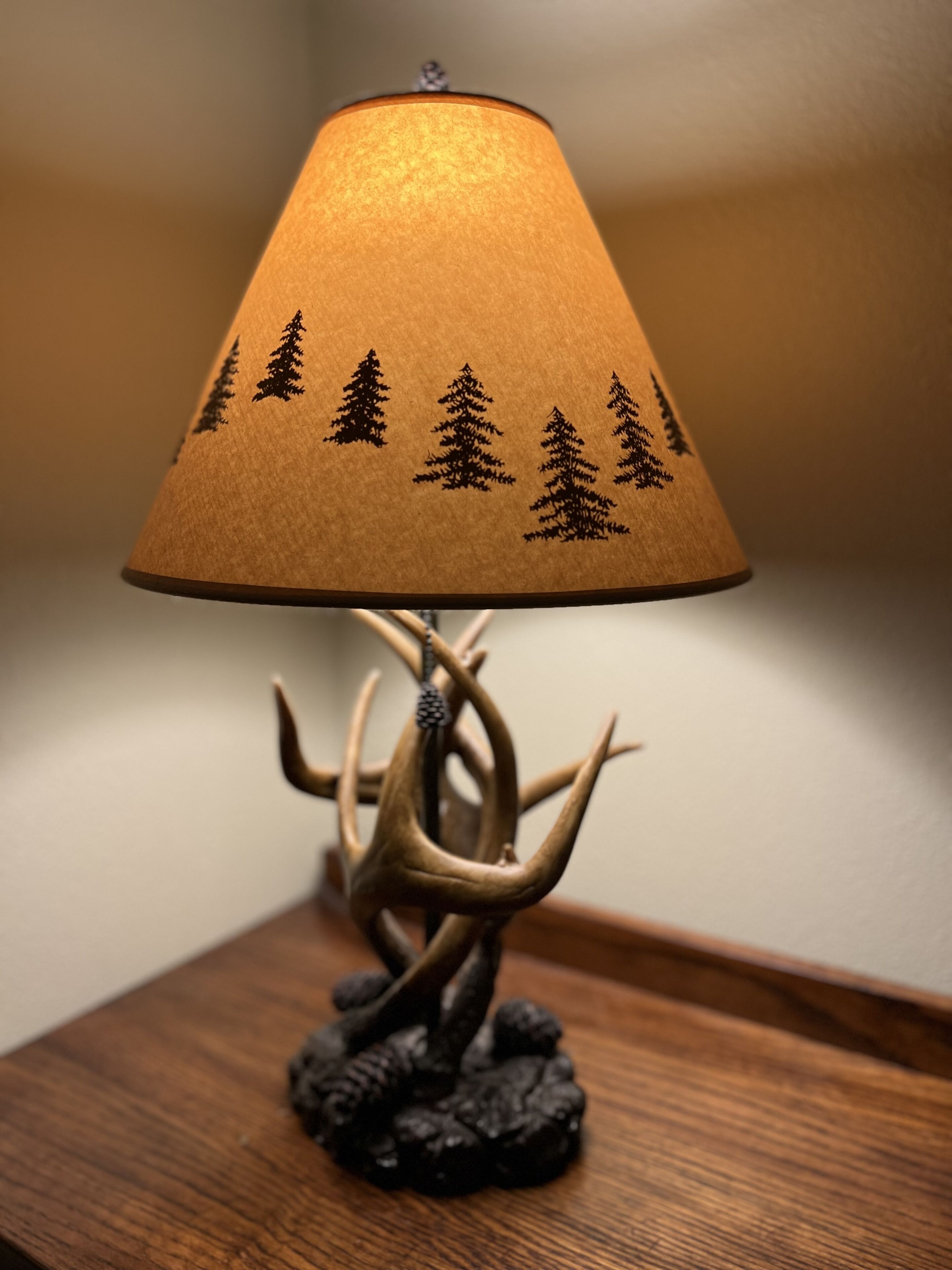 A lamp with a wooden base and a lampshade featuring tree silhouettes.