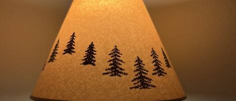 A lamp with a wooden base and a lampshade featuring tree silhouettes.