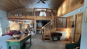 A spacious loft-style room with a high ceiling, wooden beams, a staircase, and a cozy seating area with a table and chairs. - Charming Waterfront Pine Cabin on Curlew Lake (Republic)