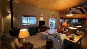 A cozy living room with a fireplace, comfortable seating, a television, and a kitchen area visible through an open door. - Charming Waterfront Pine Cabin on Curlew Lake (Republic)