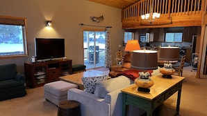 A cozy living room with a television, sofas, a coffee table, and a kitchen area visible through an open door. - Charming Waterfront Pine Cabin on Curlew Lake (Republic)