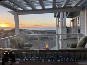 En mysig balkong med utsikt över stranden, en eldstad och en välkomnande skylt.