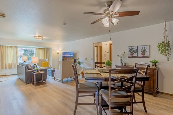 A spacious living area with a dining table, chairs, and a ceiling fan.
