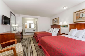 Une chambre d’hôtel avec deux lits, un bureau, une chaise, une télévision et une salle de bain visible à travers une porte ouverte.