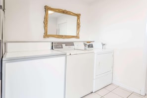 Zona de lavandería con lavadora blanca, secadora y un espejo grande en la pared.