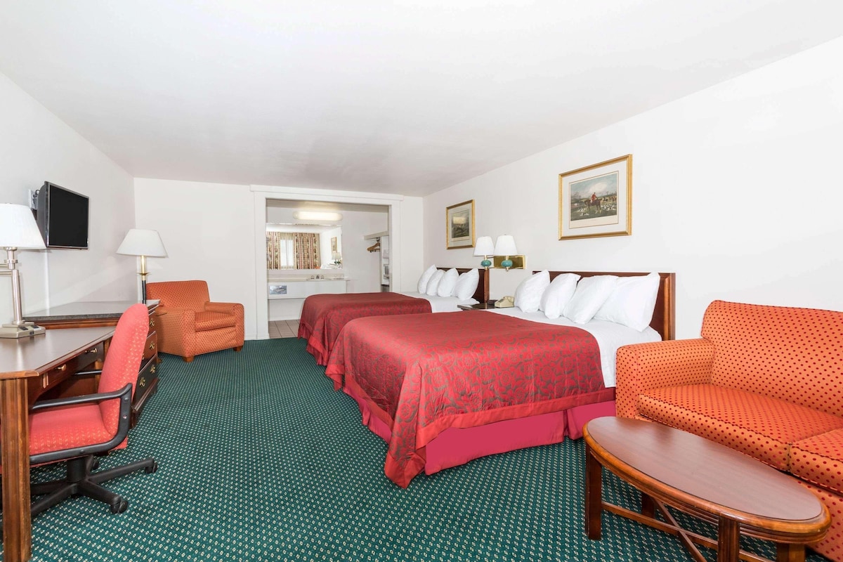 A hotel room with a desk, two beds, a sofa, and a chair.