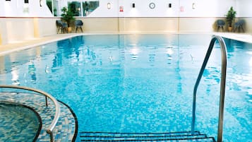 An indoor swimming pool with clear water, a metal ladder, and tiled walls.