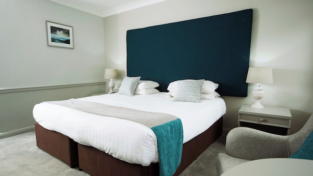 Ein Hotelzimmer mit einem großen Bett, Nachttischen, einem Sessel und einem gerahmten Bild an der Wand.