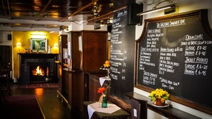 Ein Restaurantinneres mit einer Tafel, auf der Sandwiches, Salate und Getränke angeboten werden. Im Hintergrund ist ein Kamin zu sehen.