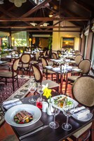 Interior de restaurante com mesas preparadas para refeições, exibindo diversos pratos e copos de vinho.