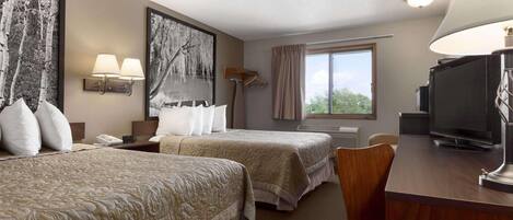 Une chambre d’hôtel avec deux lits, un bureau avec une télévision, une fenêtre avec des rideaux et des œuvres d’art accrochées aux murs.
