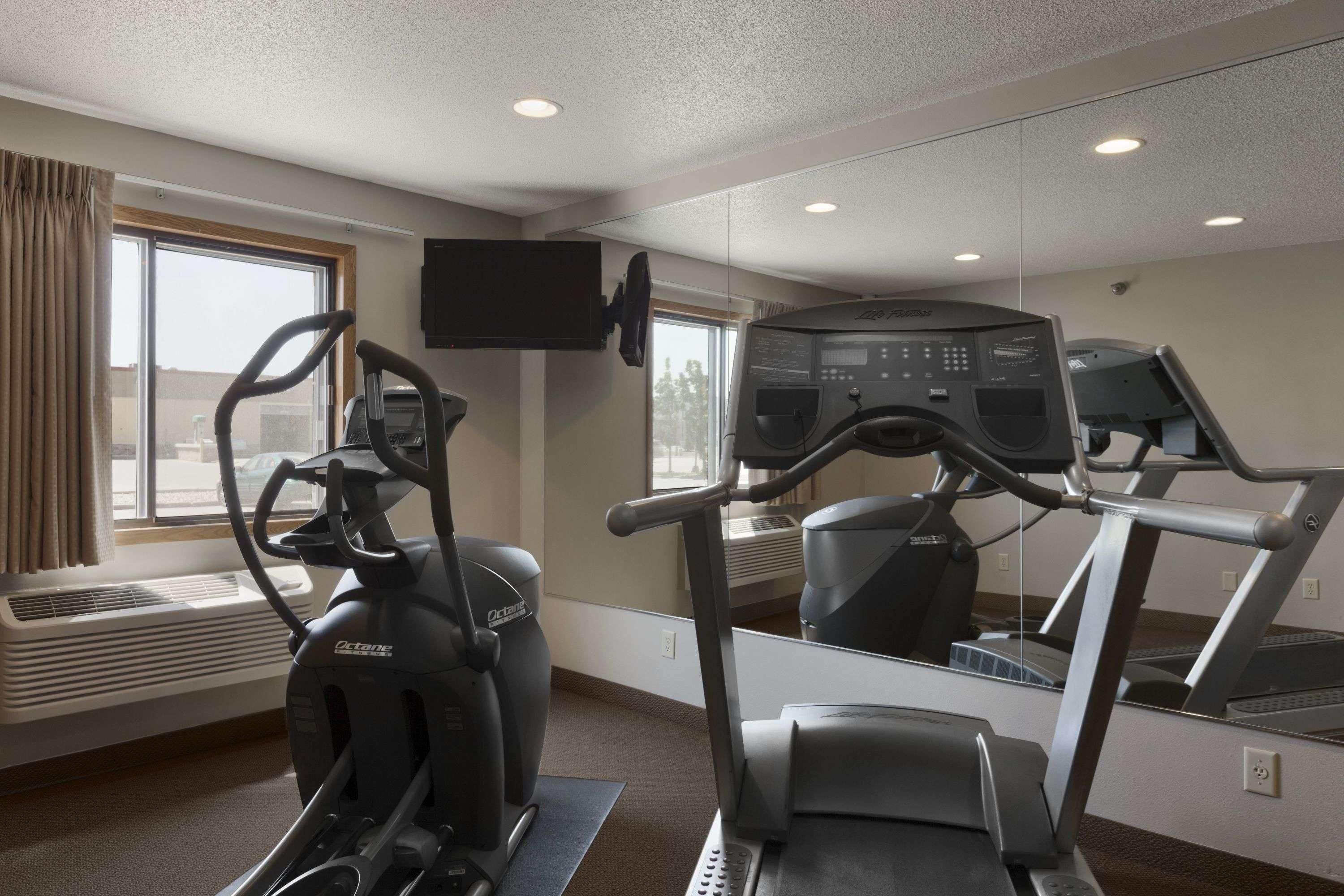 A gym with an elliptical machine, a treadmill, and a mirrored wall.