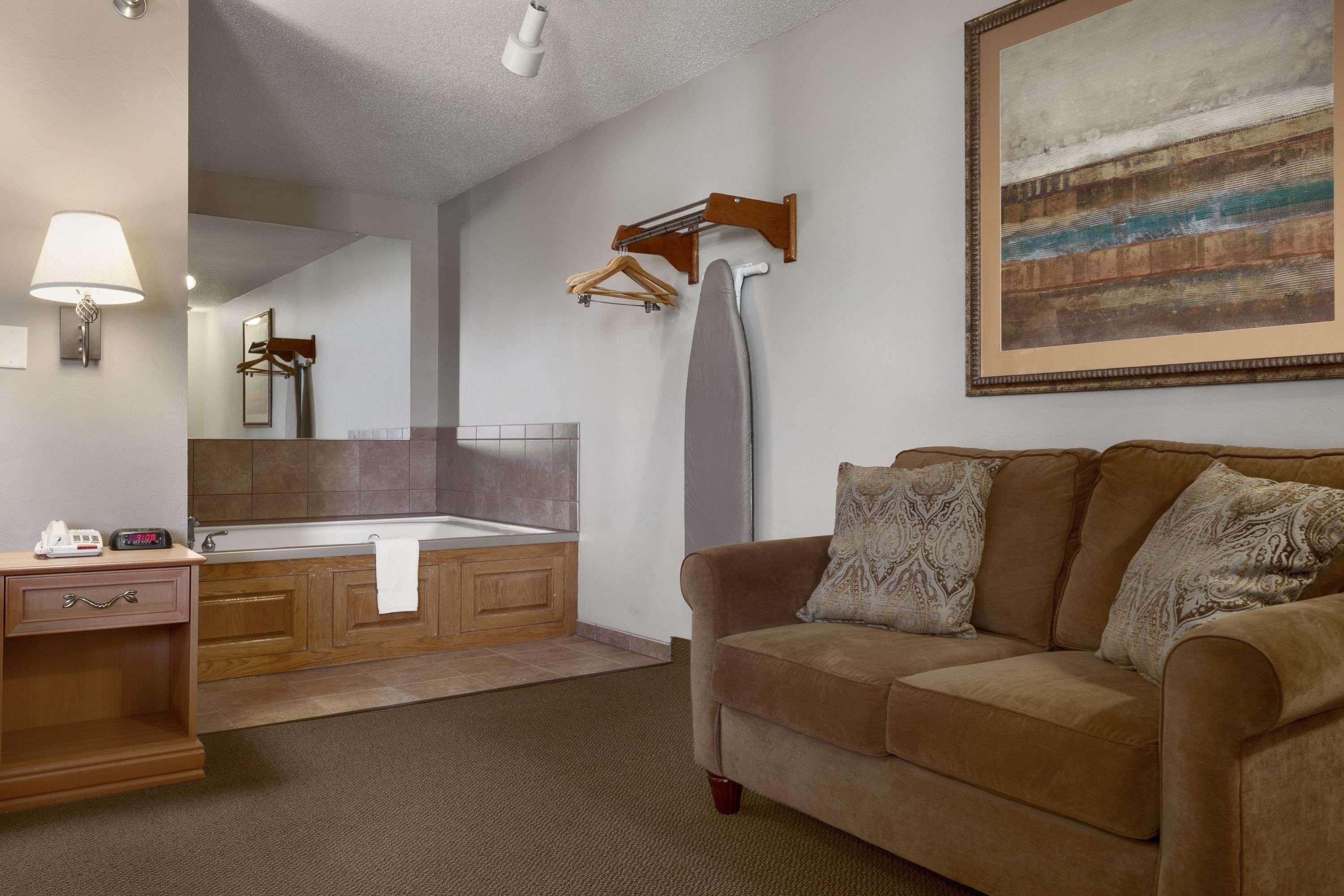A hotel room with a bathroom, a sofa, a painting, and a clock.