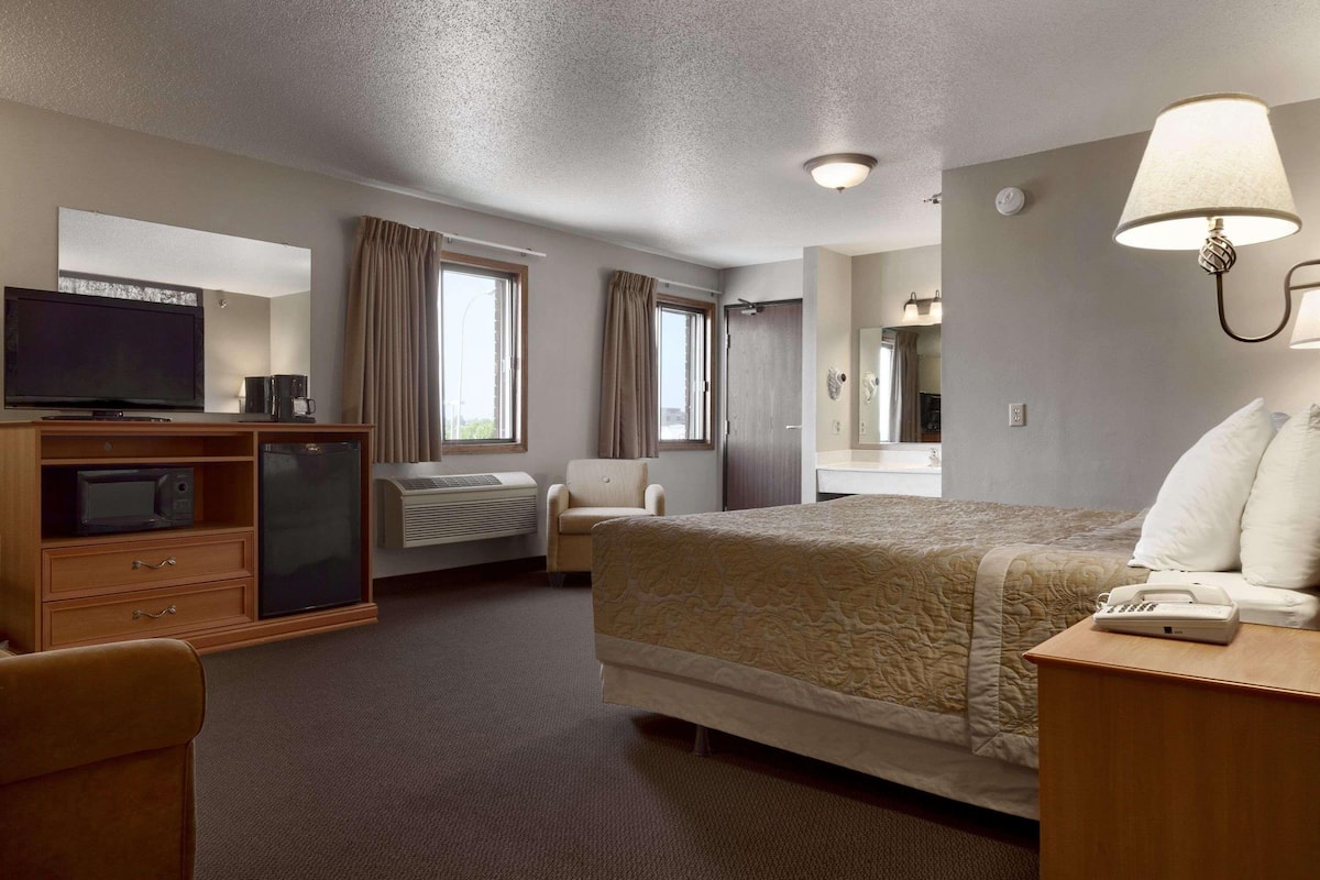 A hotel room with a bed, a desk with a telephone, a television, a minibar, a chair, and a window with curtains.