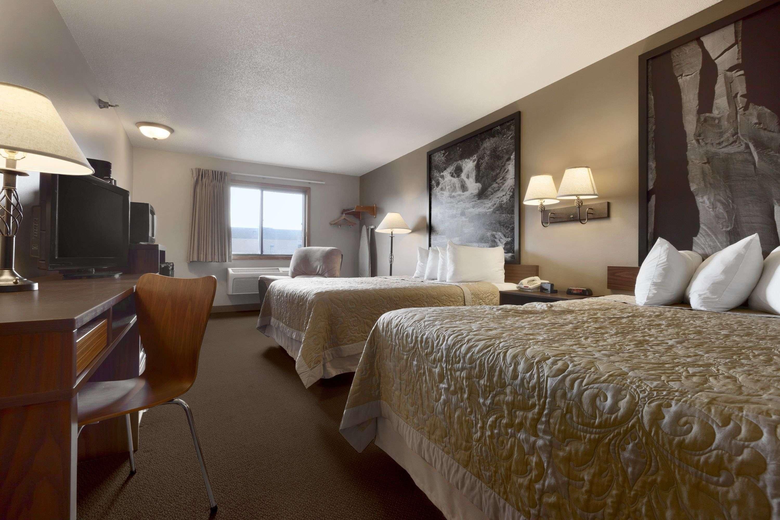 A hotel room with two beds, a desk, a chair, a television, and a large abstract painting on the wall.