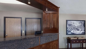 A reception area with a marble counter, wooden cabinets, and a framed picture of a waterfall. - Super 8 by Wyndham Sioux Falls/41st Street (Sioux Falls)