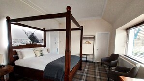 A four-poster bed with a plaid carpet, a desk with a chair, and a coat rack in a hotel room.