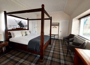 A four-poster bed with a plaid carpet, a desk with a chair, and a coat rack in a hotel room. - The Four Seasons Hotel (Crieff)