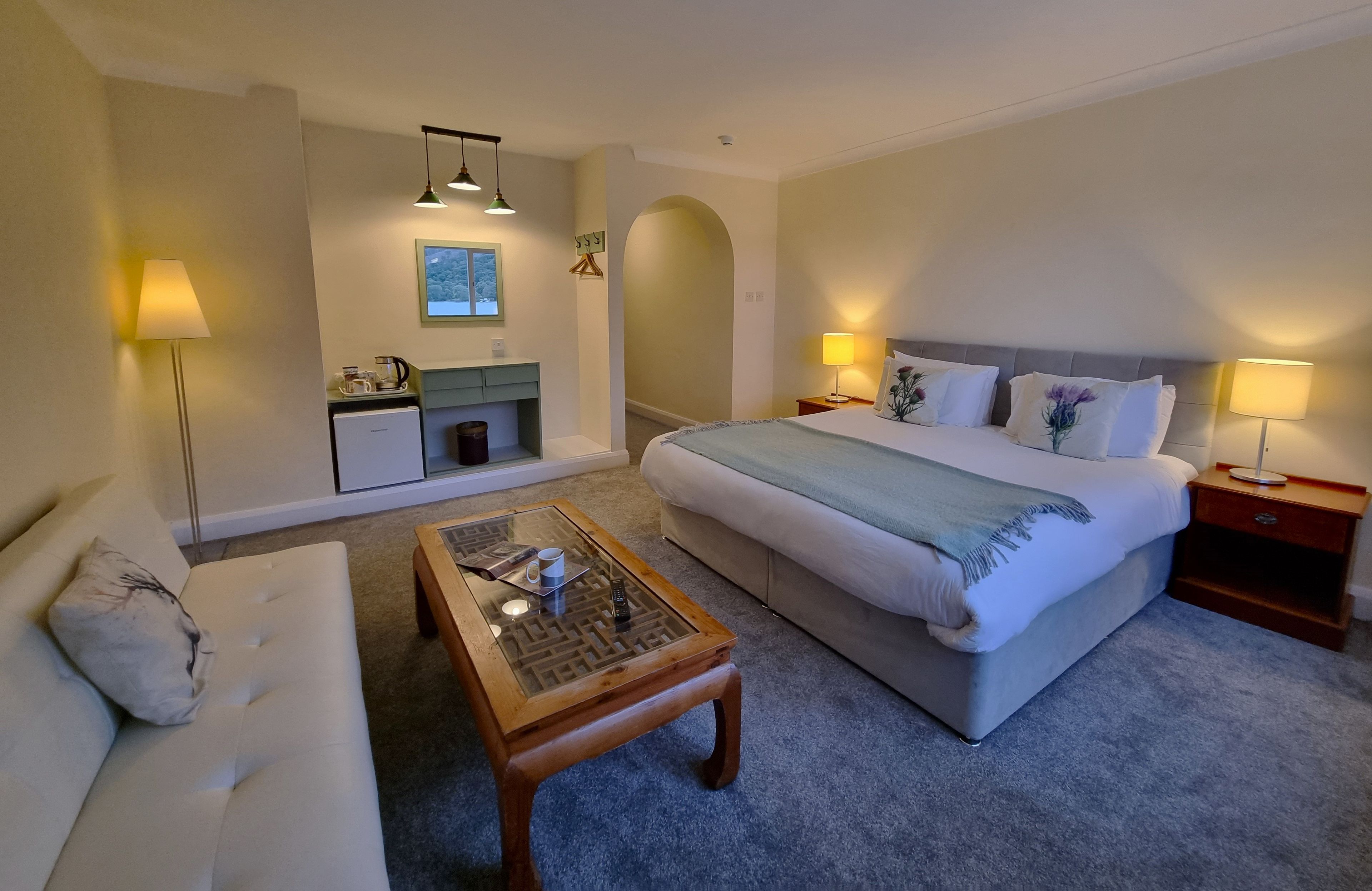 Una habitación de hotel con cama, sofá, mesa de centro, escritorio y lámpara.