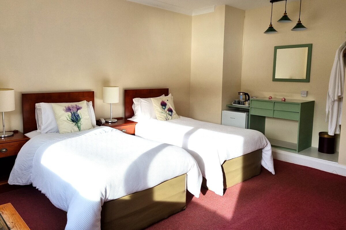 A hotel room with two beds, a desk, a vanity, and a mirror.