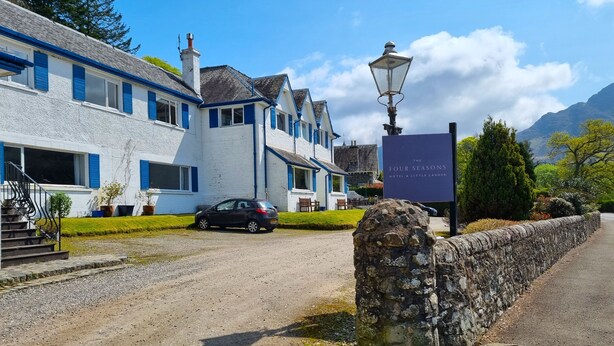 Ein traditionelles weißes Gebäude mit blauen Fensterläden, einer Steinmauer und einem Schild für The Four Seasons Hotel & Little Larder.