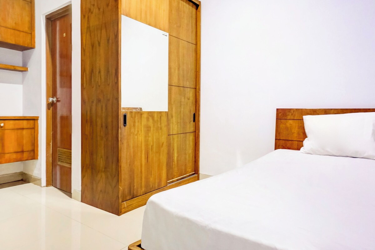 Un dormitorio con un armario de madera, una cama con colchón blanco y cabecera de madera.