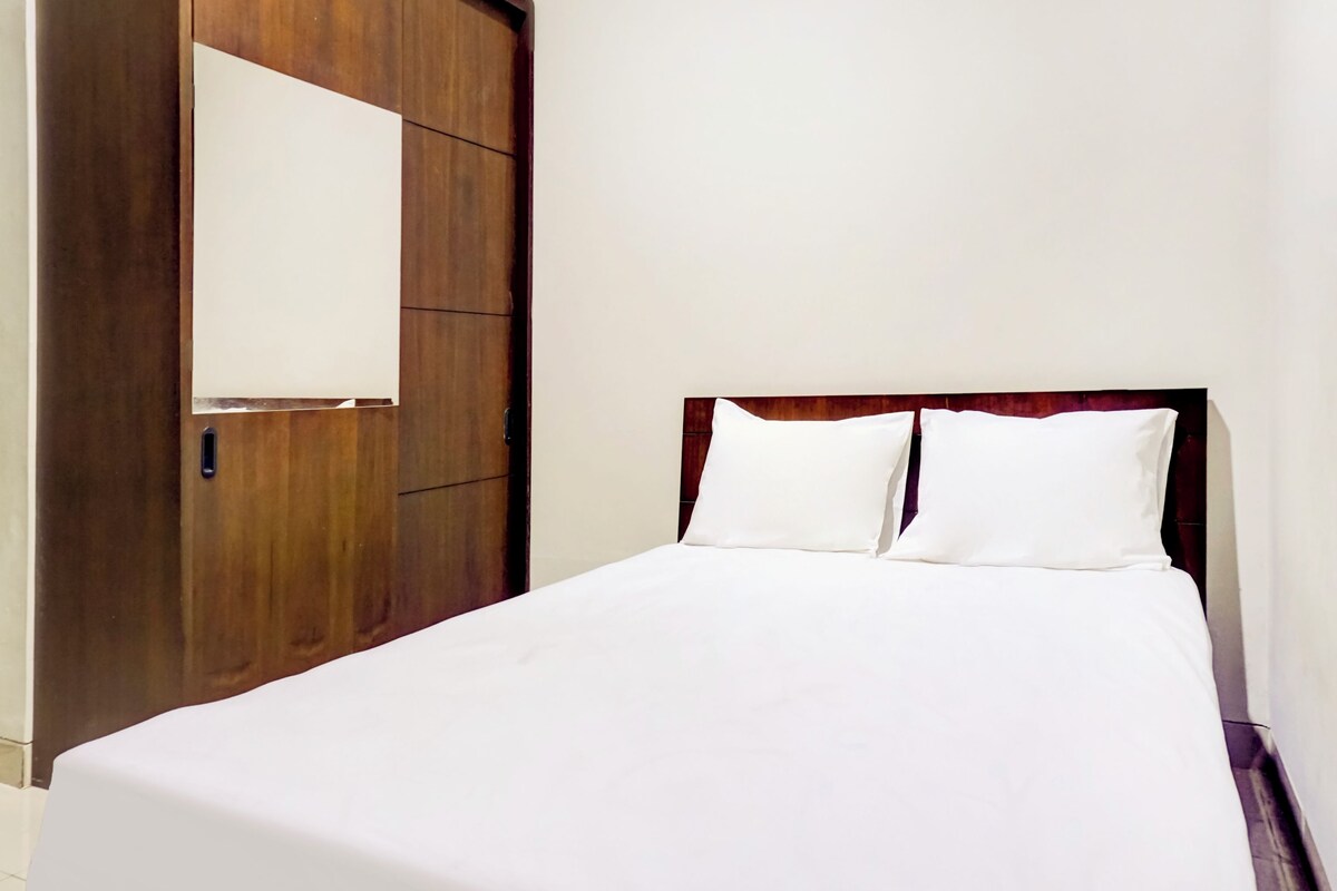 Habitación de hotel con armario de madera, cama con ropa blanca y pared lisa.
