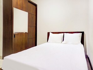 Habitación de hotel con armario de madera, cama con ropa blanca y pared lisa.